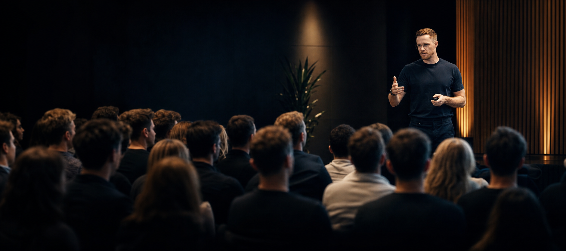 Ant Milner speaking to a seated audience in a dark auditorium